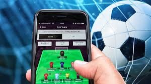 Someone is playing fantasy football sports game on mobile using app. Thhe green field is visible. In the background a huge football image could be seen.