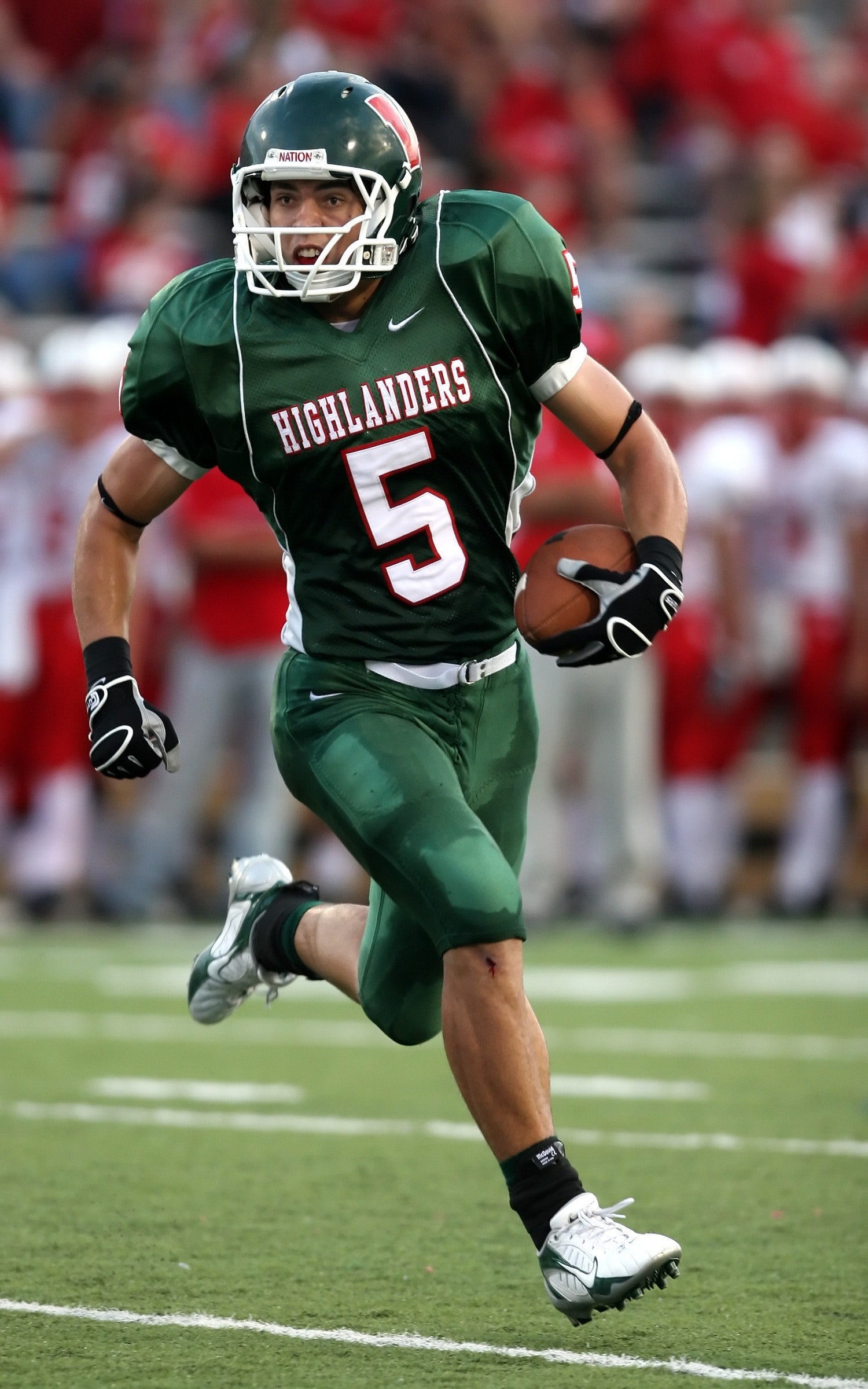 An American footballer in green suit running with the football in his left hand during a tournament